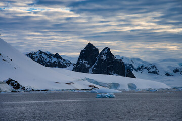 Antarctic Peninsula: Snowy peaks, icebergs, cloudy sky. Lemaire Channel