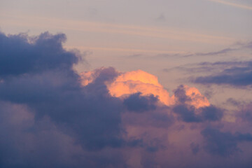 Dramatic sunset clouds with vibrant orange glow, surrounded by soft purples and blues, creating serene sky scene