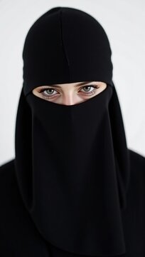 A portrait of a young Middle-Eastern woman in a black niqab, showcasing her expressive eyes and cultural attire against a neutral background, highlighting tradition and modesty.