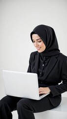 Portrait of a Young Muslim Woman in a Black Hijab Working on a Laptop in a Professional Setting, Showcasing Modern Workplace Dynamics
