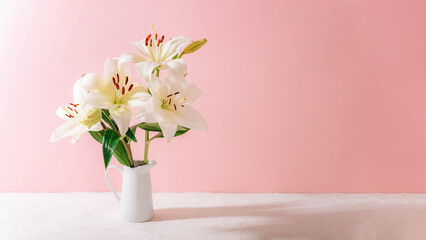 White lilies in a ceramic vase on a pastel pink background with soft shadows