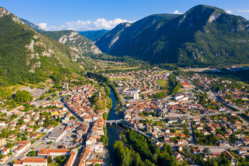 View from drone of small French town of Tarascon-sur-Ariege on banks of Ariege river in valley of Pyrenees on background of summer mountain landscape