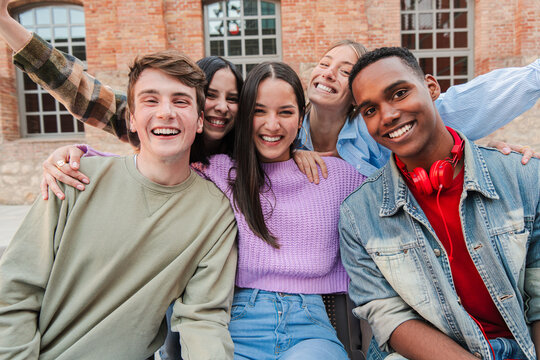 Joyful group of five young friends smiling brightly while posing together for a fun photo, showcasing their happiness and connection in a lively gathering filled with laughter and excitement