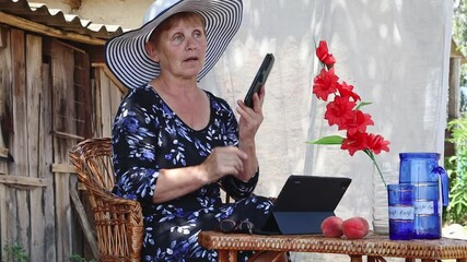 An elderly woman is talking on a mobile phone in the garden.
