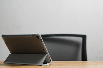 A tablet placed on a stand, positioned on a wooden desk, with an office chair in the blurred...