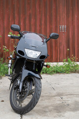 Black motorcycle parked in front of a wooden fence on a concrete surface
