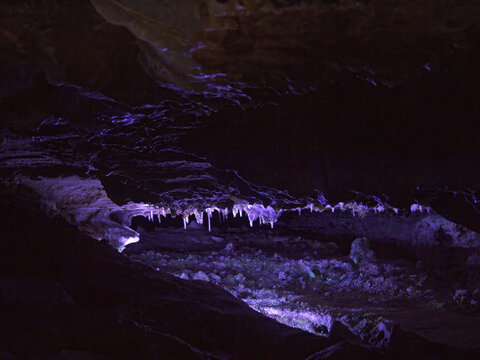Dark cave with stalactites illuminated with flashlight