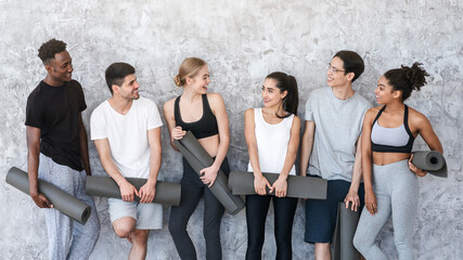 Fototapeta premium Healthy Lifestyle Concept. Group of sporty people with yoga mats resting after class near grey wall in fitness studio