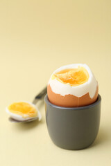 Soft boiled egg in eggcup and spoon on beige background, closeup
