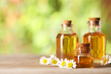 Bottles of essential oil and chamomile flowers on wooden table, closeup. Space for text