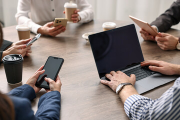 Group of people using different gadgets at wooden table in office, closeup. Modern technology