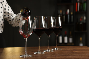 Professional sommelier pouring red wine into glasses at wooden table indoors, closeup