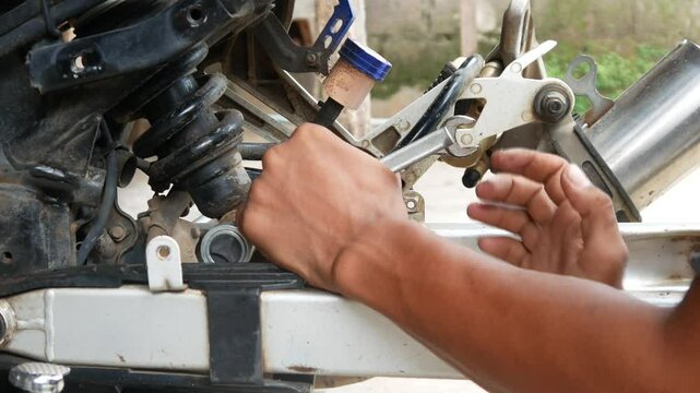 A mechanic's hand opens a motorcycle shockbreaker bolt for maintenance, repair and service