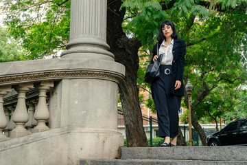 Elegant latin businesswoman walking down stone stairs in urban park