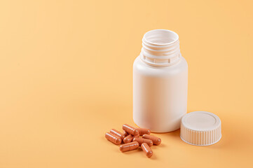 Bottle of medical capsules pills on light orange background.
