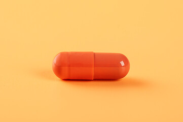 Orange capsule pill on yellow background.