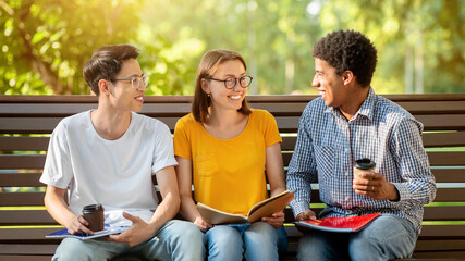 Students Lifestyle Concept. Three Multicultural Millennials Talking Sitting On Bench Outside...