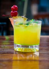 Close-up view of a vibrant Tequila Sunrise cocktail with pineapple and maraschino cherries, showcasing the colorful details inside the glass.
