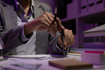 A woman is sitting at a desk with two model houses in front of her. She is holding a pencil and she...