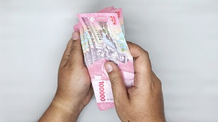 two hands counting Indonesian banknotes in the 100,000 rupiah denomination