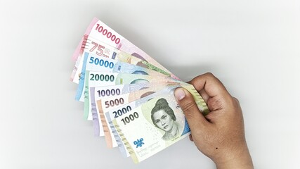 hand holding a collection of Indonesian banknotes in denominations 1000, 2000, 5000, 10000, 20000, 50000, 75000, 10000 rupiah