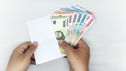 two hands take out a collection of Indonesian banknotes from a white envelope. denominations of 1000, 2000, 5000, 10000, 20000, 50000, 75000, 10000 rupiah