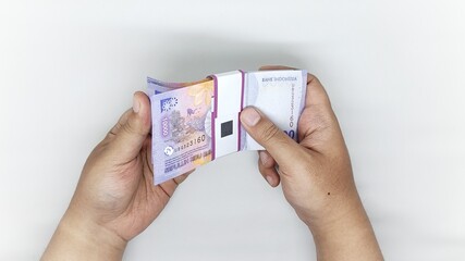 two hands counting Indonesian banknotes in the 10,000 rupiah denomination