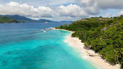 Obraz premium A white sandy beach with clear turquoise water, bordered by dense green vegetation. Therese. Seychelles, Mahe.