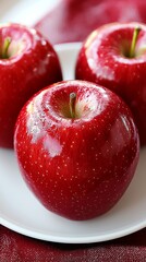 Fresh red apples glistening on a white plate with a textured red background