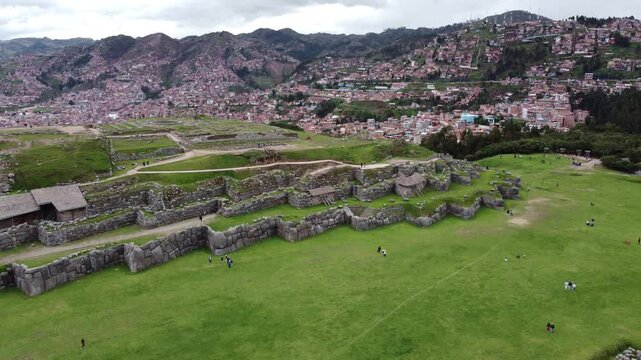 Tourists walking around sacsayhuaman fortress walls with cusco city in background