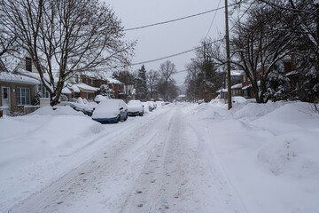 Row of cars parked and stuck on residential unplowed street due to large amount of accumulated snow during heavy snowstorm in Toronto, Ontario, Canada. Severe weather and unsafe driving conditions.