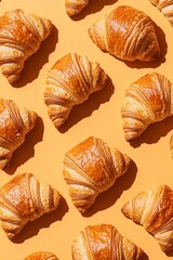 Golden croissants are beautifully arranged across a bright orange surface, offering a mouthwatering view that invites indulgence. Each flaky layer is a testament to culinary craftsmanship