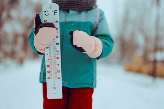 Little Girl Holding Thermometer Showing Freezing Temperatures. Kid demonstrating how cold a winter day really is 
