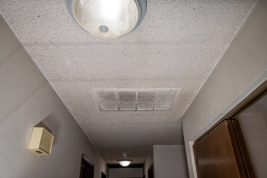Large white air intake vent in hallway ceiling covered in dust and cobwebs along with asbestos containing popcorn ceiling, rental home interior dirty mess after the tenant moves out, housing market

