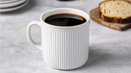 A steaming cup of black coffee beside a slice of bread on a textured surface