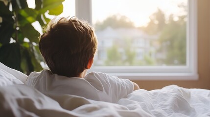 Young boy lying in bed while gazing out the window at the warming morning light and peaceful surroundings : Generative AI