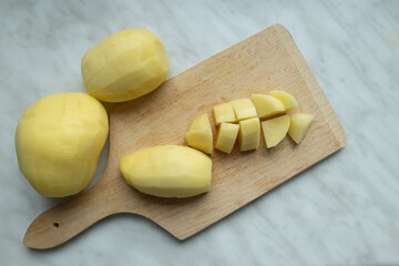 A close-up of peeled and diced potatoes on a wooden cutting board.
