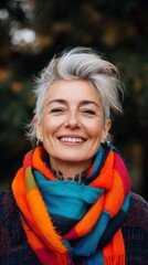 Fototapeta premium Joyful woman with gray hair and vibrant scarf smiling in a natural setting during autumn