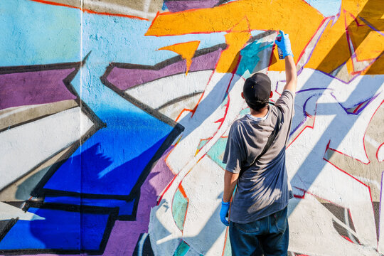 Street artist using aerosol can to create vibrant graffiti art on urban wall