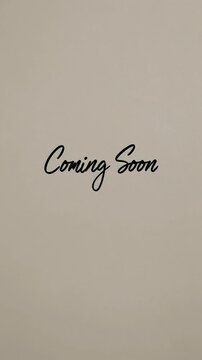 Minimalist 'Coming Soon' video concept with a neutral background and elegant script font. Straight-on camera angle enhances simplicity and focus. Suitable as mobile wallpaper.