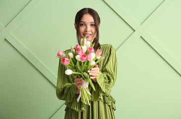 Pretty young Asian woman with bouquet of beautiful tulips on green background. International...