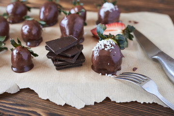 Chocolate dipped strawberries with coconut and mint on a wooden background.