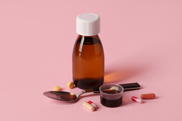 Bottle and measuring cup of cough syrup with different pills on pink background