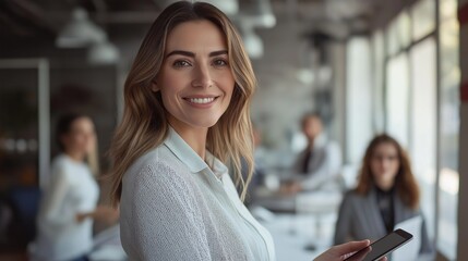 A confident business leader smiles warmly as she engages with her colleagues in a contemporary office space filled with natural light. The atmosphere is vibrant and interactive