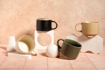 Different ceramic mugs with plaster podiums on beige tile table