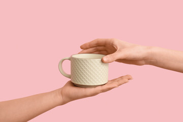Female hands with white ceramic mug on pink background