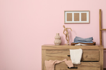 Commode with scattered clothes near pink wall in living room, closeup