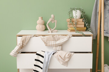 Commode with scattered clothes near green wall in living room, closeup