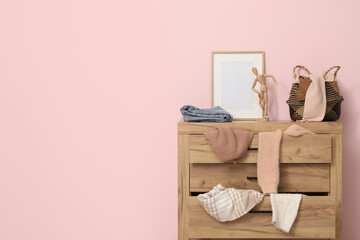 Commode with scattered clothes near pink wall in living room