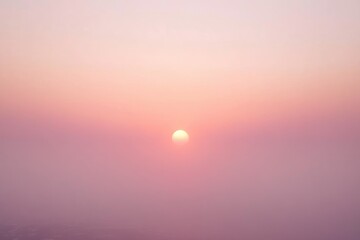 A hazy, pink sunset with a soft, muted sun centered in the frame.